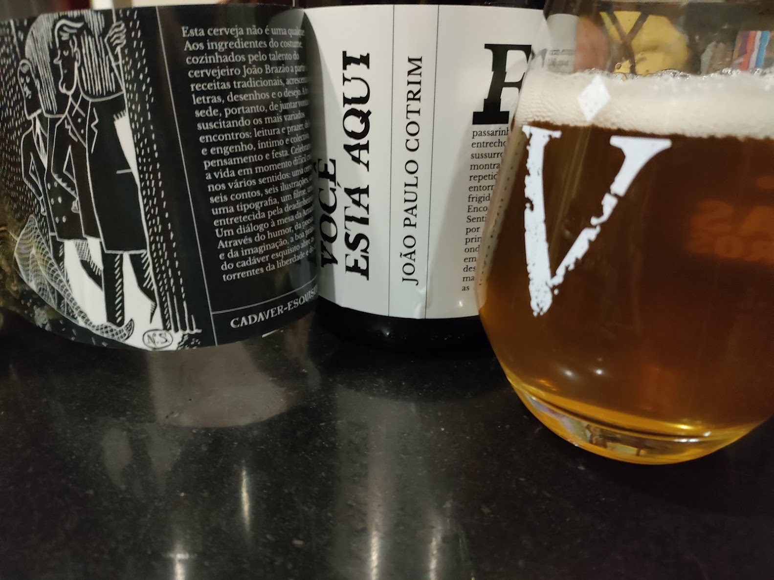 Garrafa Você está aqui, de João Paulo Cotrim, com o rótulo desdobrado, ao lado de um copo de cerveja
